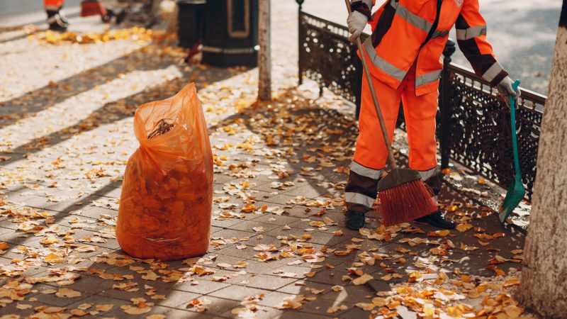 Ein Arbeiter reinigt den Gehweg von Laub